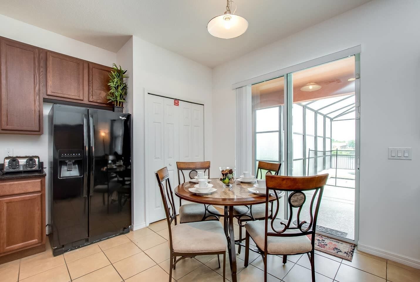 A modern kitchen with a stainless steel refrigerator, wooden cabinets, and a dining area with a round table and chairs.