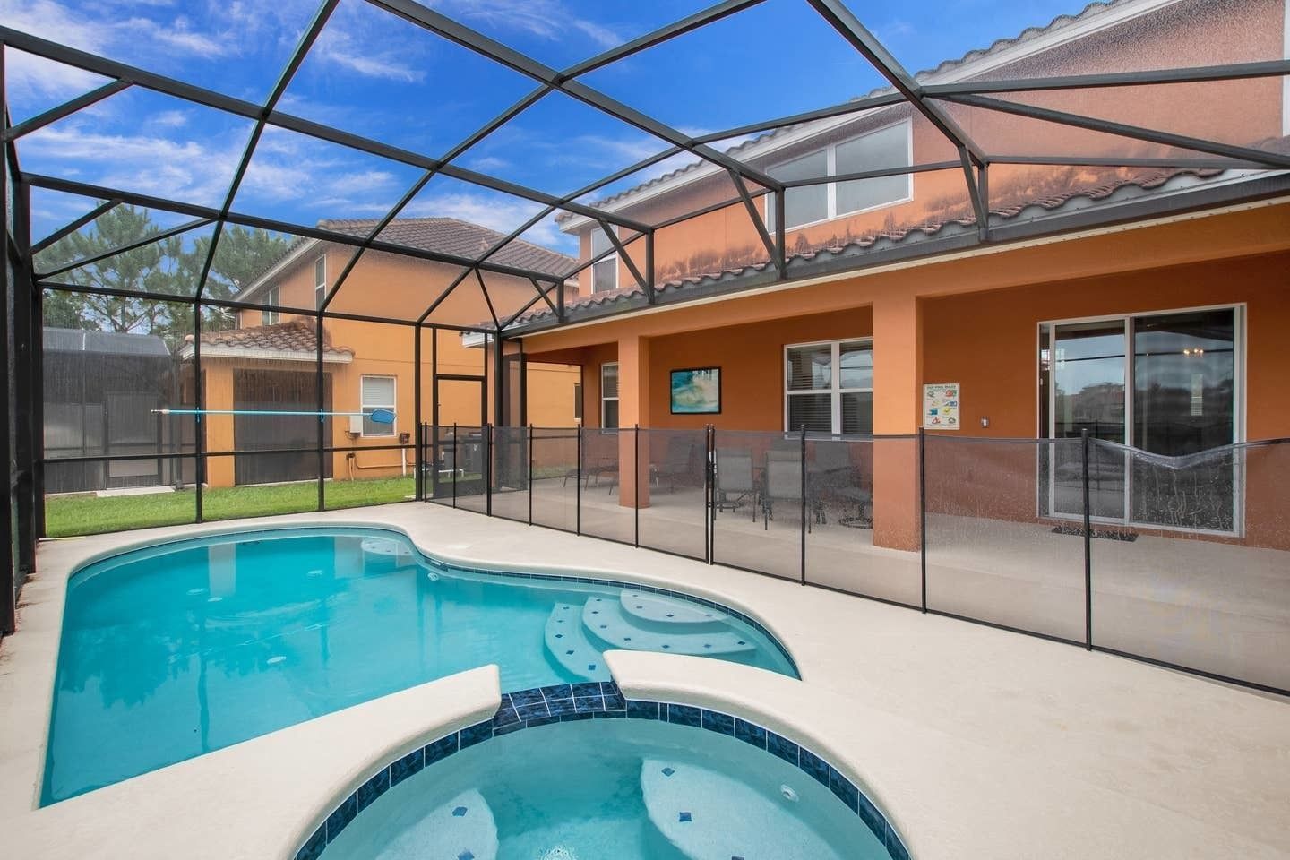 A swimming pool with a hot tub, enclosed by a glass fence, and a covered patio area.