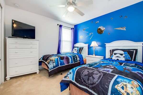 A bedroom with two beds, a TV, a ceiling fan, and a wall with Star Wars-themed decorations.
