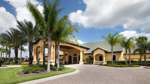 A hotel with a yellow facade, palm trees, and a paved entrance.