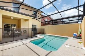 Una piscina con cerramiento de vidrio, un área de patio con mobiliario exterior y vistas al vecindario.