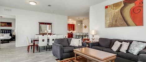 A modern living room with a gray sofa set, a wooden coffee table, and a dining area with a white table and chairs.