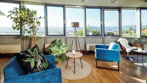 A modern living room with a large window, a blue sofa, a coffee table, and a view of the landscape. - Michel Hotel Karoli Waldkirchen (Waldkirchen)