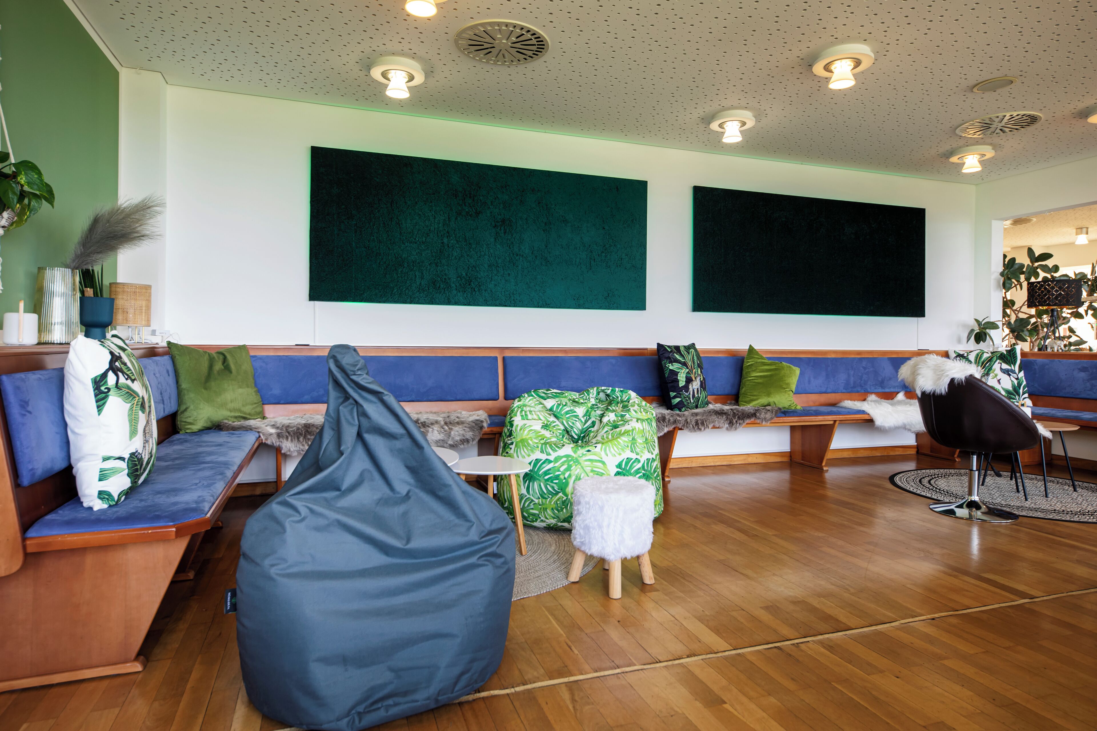 Een moderne lounge met houten vloer, een blauwe bank met groene en witte kussens, een grijze relaxstoel en een zwarte fauteuil.