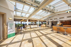 Un vaste espace intérieur doté d’un haut plafond et de lucarnes, comprenant un bar avec des tabourets et un comptoir d’accueil.