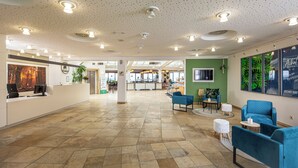 A spacious lobby with a reception desk, seating area, and a view of the kitchen in the background. - Michel Hotel Karoli Waldkirchen (Waldkirchen)