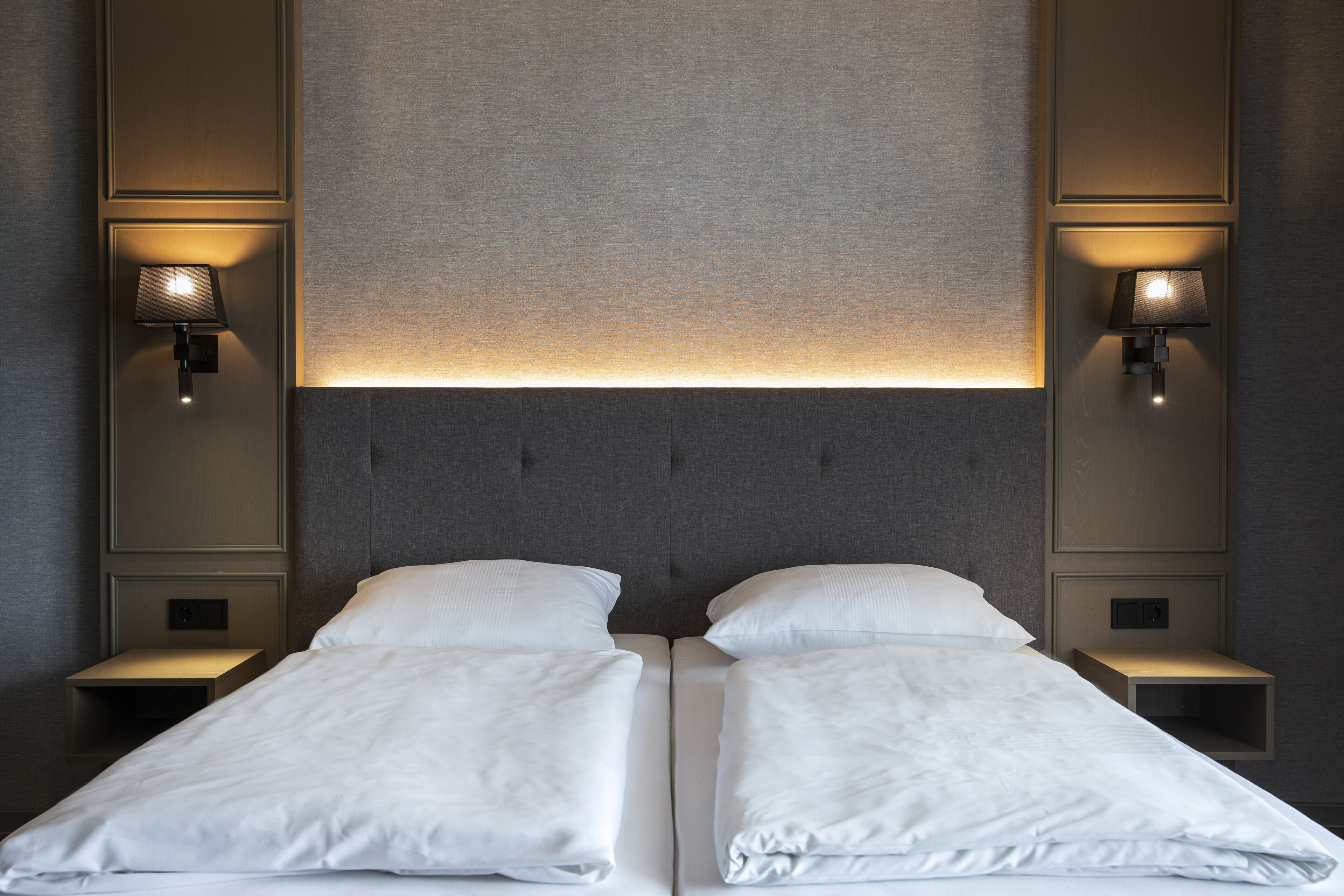 A double bed with white linens, two bedside tables, and wall-mounted lamps.