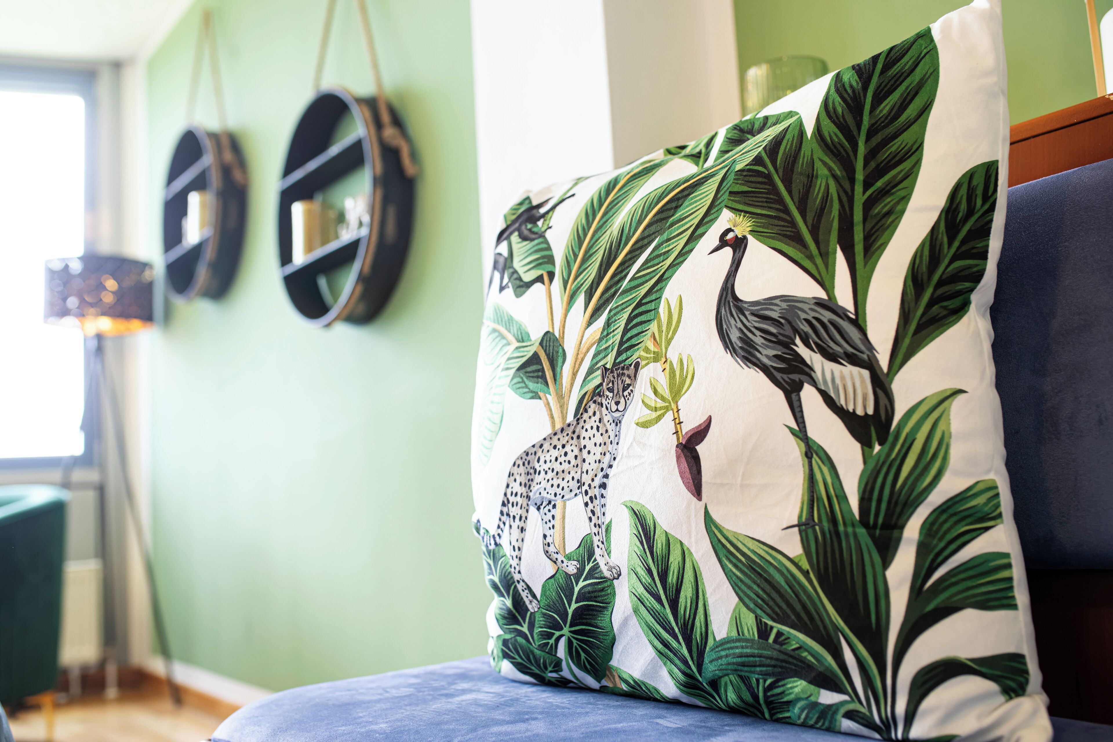A room with a green wall, a blue sofa, and a decorative pillow with a jungle print.
