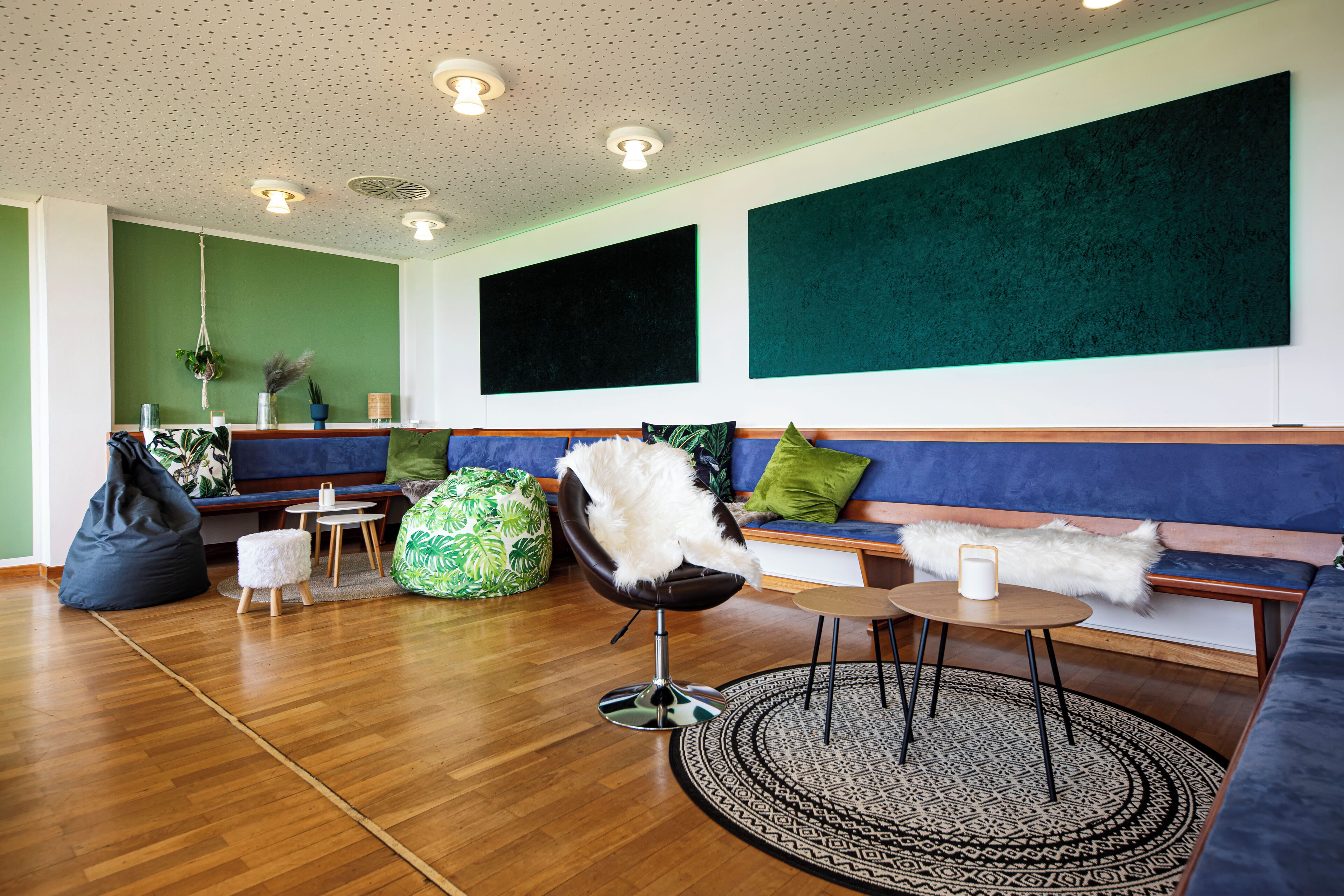 A modern living room with a wooden floor, a blue sofa, a black chair, and a green bean bag.