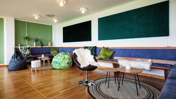 A modern living room with a wooden floor, a blue sofa, a black chair, and a green bean bag.