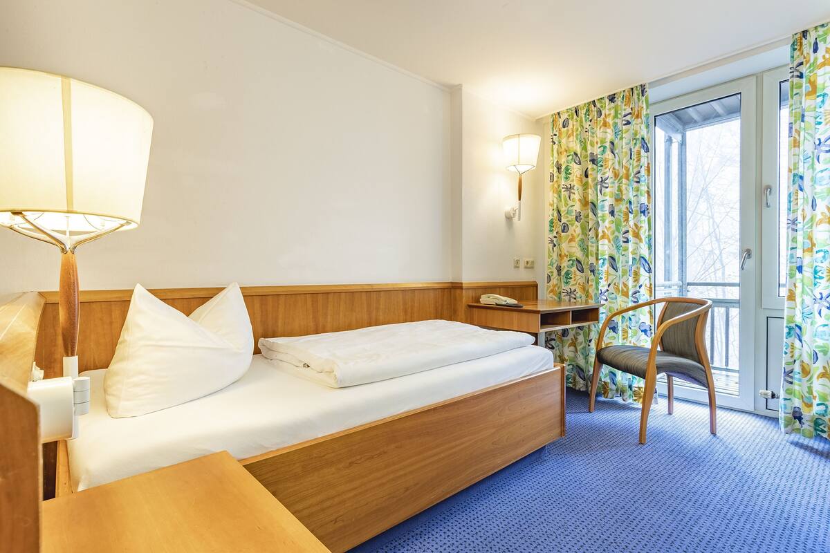 Une chambre d’hôtel avec un lit en bois, un bureau, une chaise et une fenêtre avec des rideaux.