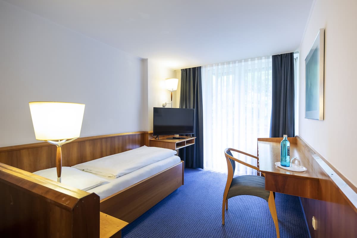 Une chambre d’hôtel avec un lit, un bureau doté d’une lampe, une télévision et une fenêtre avec des rideaux.