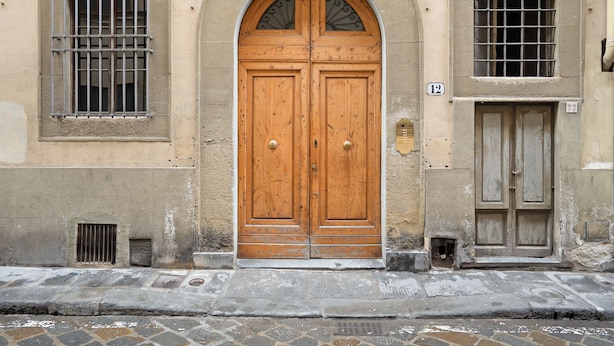 Une porte en bois à deux battants, surmontée d’une petite fenêtre, une fenêtre grillagée à gauche et une porte plus petite à droite.