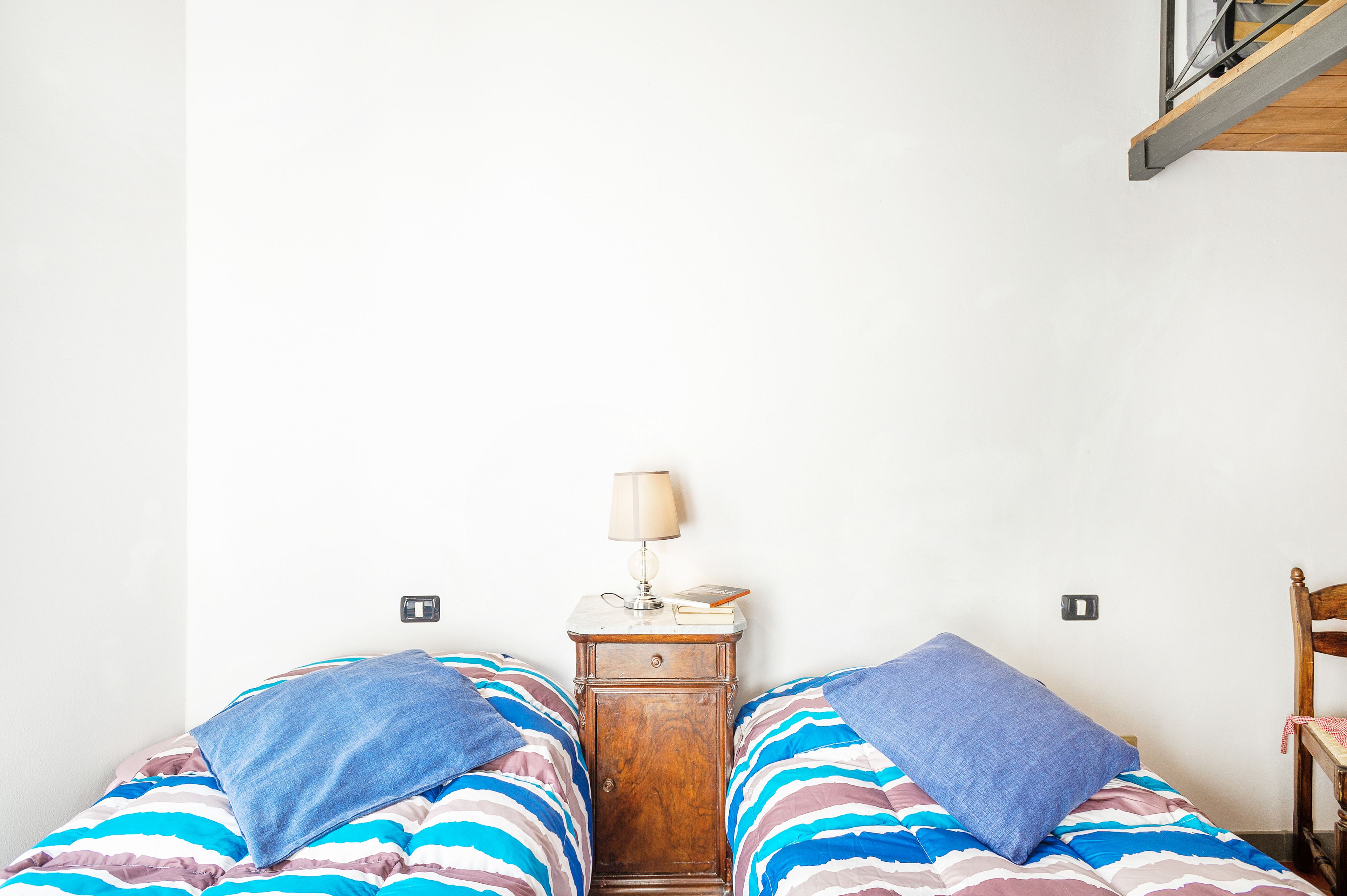 Un dormitorio con dos camas, una mesita de noche con lámpara y una silla de madera.