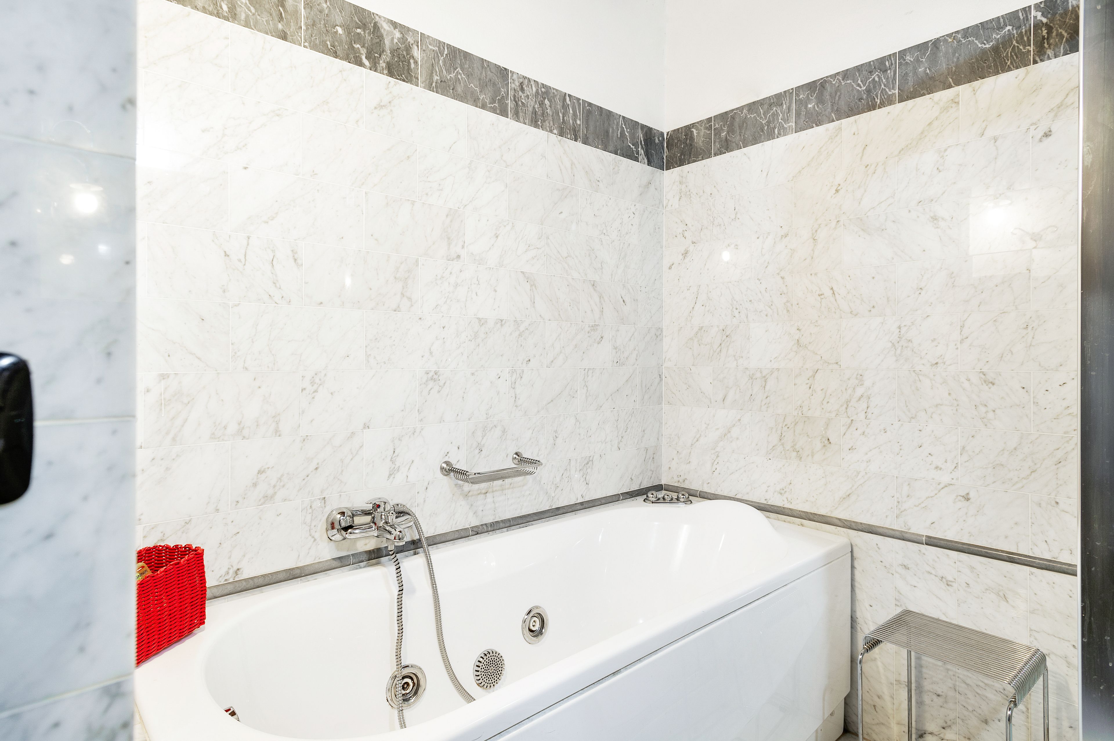 A modern bathroom with a white bathtub, chrome fixtures, and marble walls.