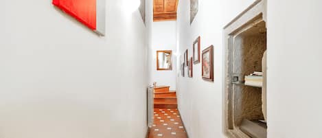 Un pasillo estrecho con suelo de baldosas, una escalera de madera y un objeto rojo en la pared.