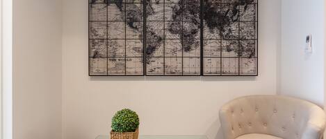 A room with a glass coffee table, a potted plant, a cushioned armchair, and a world map on the wall.