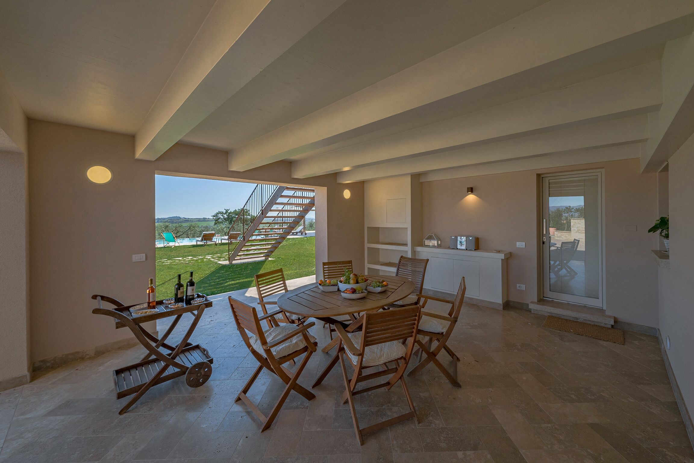 Un'ampia sala da pranzo con un tavolo rotondo e sedie, vista su piscina e giardino, e una scala che dà all'esterno.