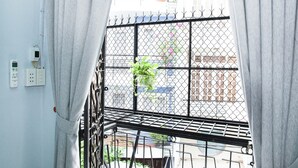 En balkon med gelænder, en potteplante og udsigt til bygninger.