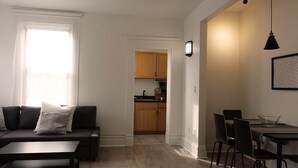 Una sala moderna con sofá, una mesa de comedor con sillas y una cocina con armarios de madera y un fregadero.