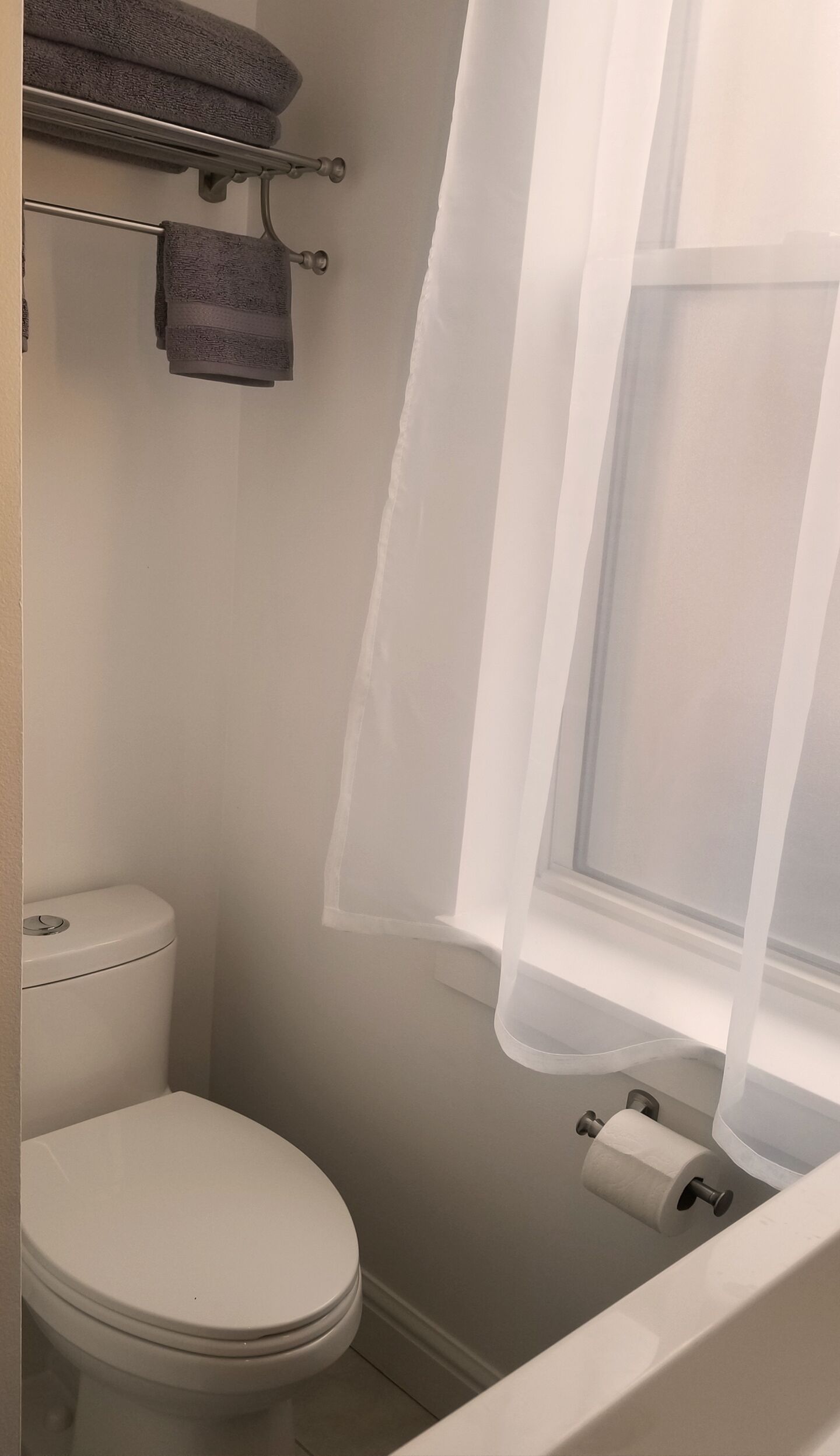 Un baño pequeño con inodoro, toallero con toallas dobladas y dispensador de papel higiénico.