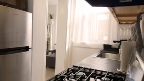 Una cocina moderna con un refrigerador de acero inoxidable, estufa a gas y una ventana con cortinas translúcidas.