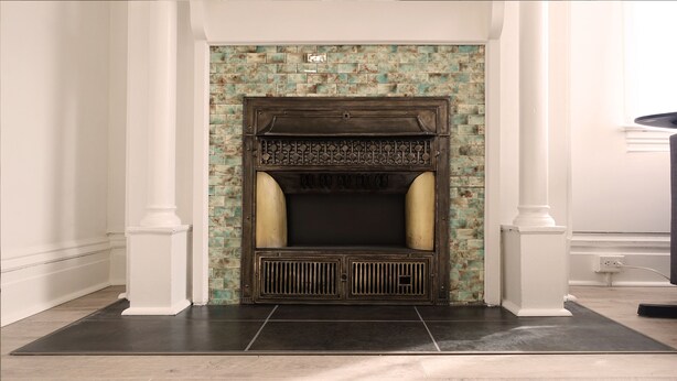Una chimenea con detalles de azulejos y repisa, ubicada en un pasillo con columnas blancas y piso de baldosas.