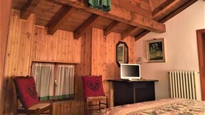 Una habitación acogedora con paredes de madera y techo inclinado, que incluye una cama, un escritorio con computadora, una silla y un radiador.