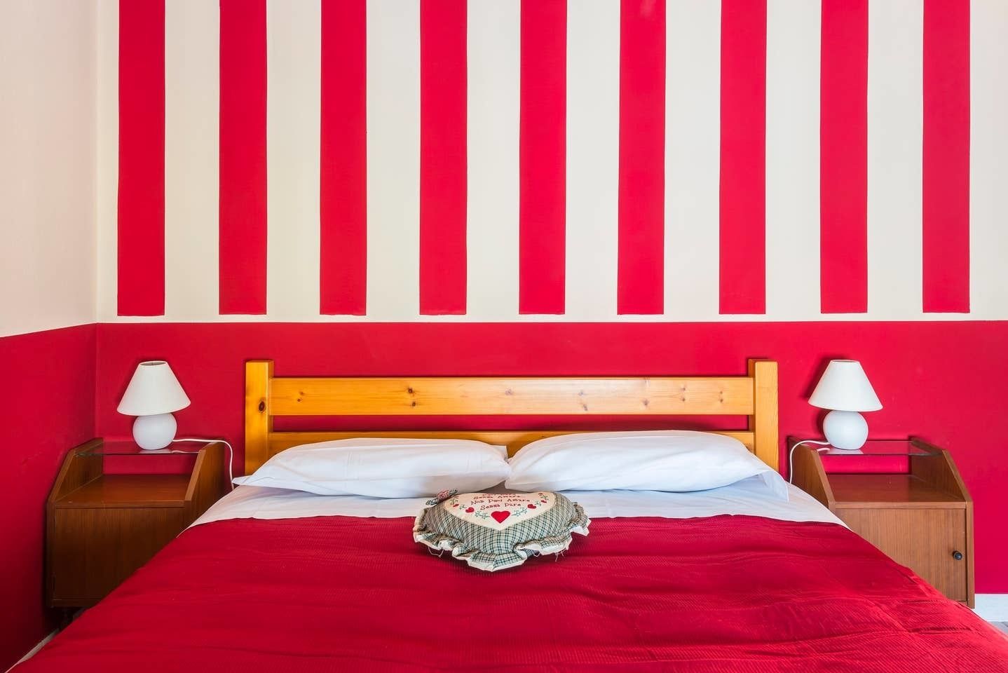 A bed with a red headboard, white pillows, and a red blanket. There are two bedside tables with lamps.
