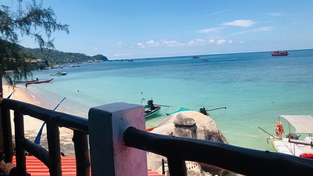 A beach with clear turquoise water, boats, and a distant ship. - Koh Tao My Hostel (Koh Tao)