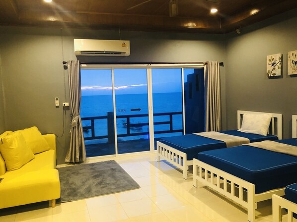 A hotel room with a balcony, a yellow sofa, two beds, and an air conditioning unit.