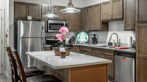 A modern kitchen with stainless steel appliances, a granite countertop, wooden cabinets, and a bar stool area. - ✪ Hidden Valley ✪ FREE Parking, Pool & Gym! (Ooltewah)