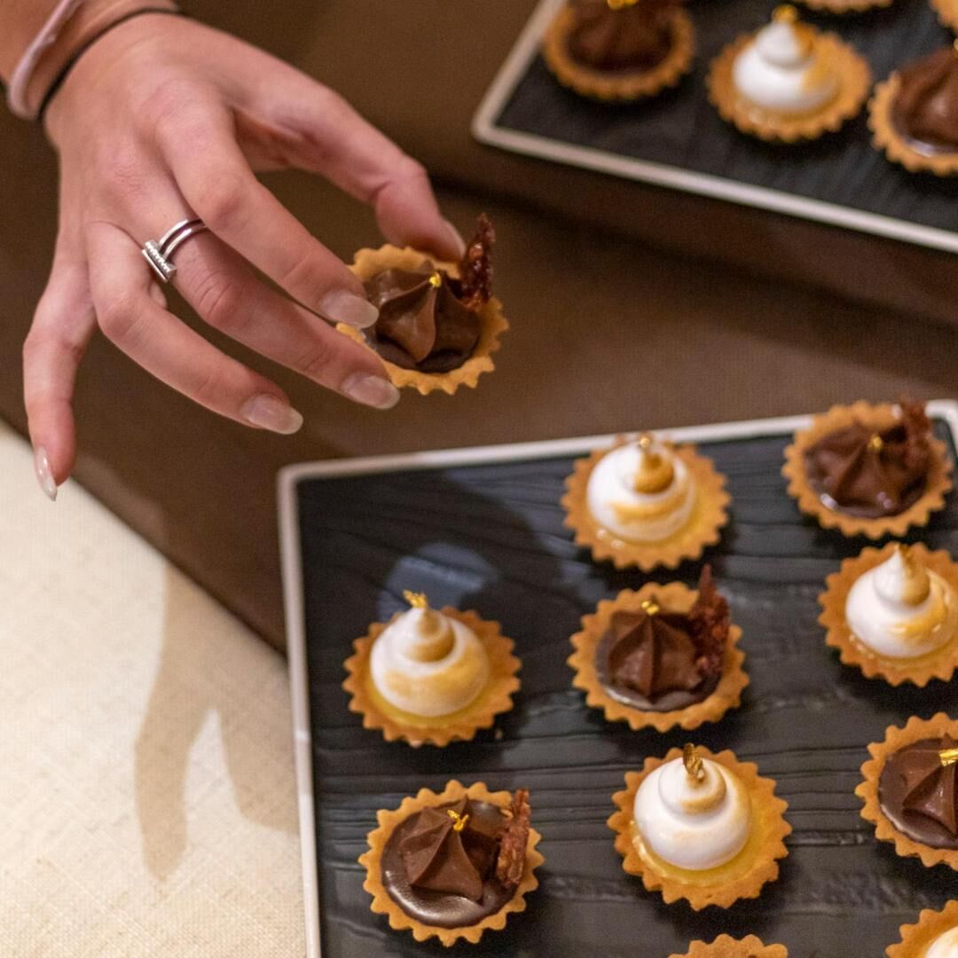 En hånd holder en chokoladetærte med bladguld på en tallerken med et udvalg af desserter.
