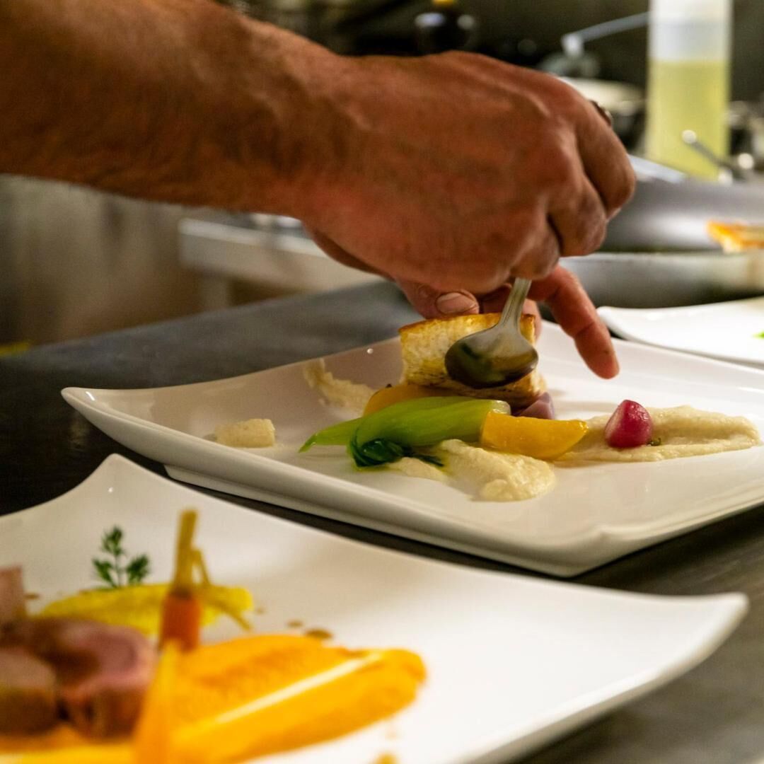 A hand holding a spoon over a dish with various food items.