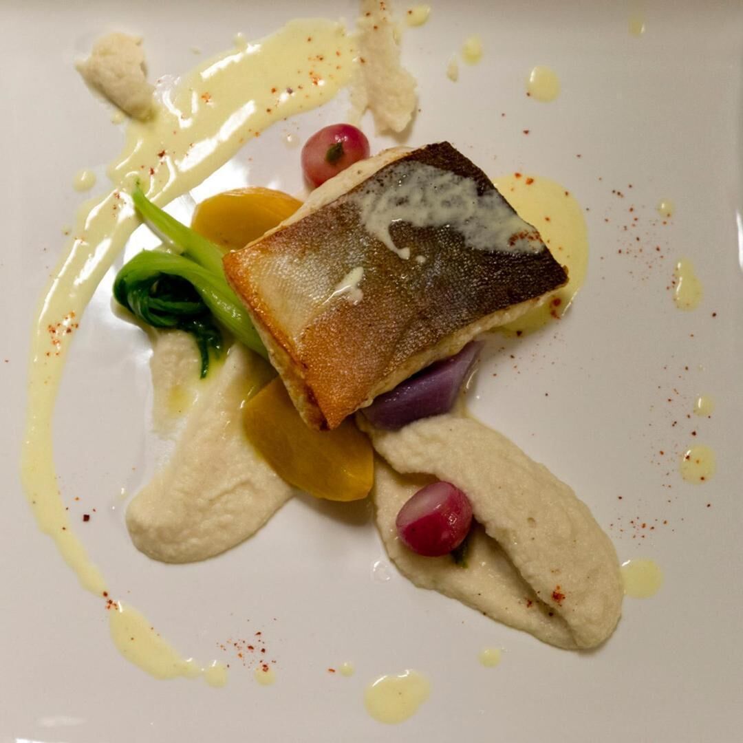 A plate with a piece of fish, vegetables, and a creamy sauce.