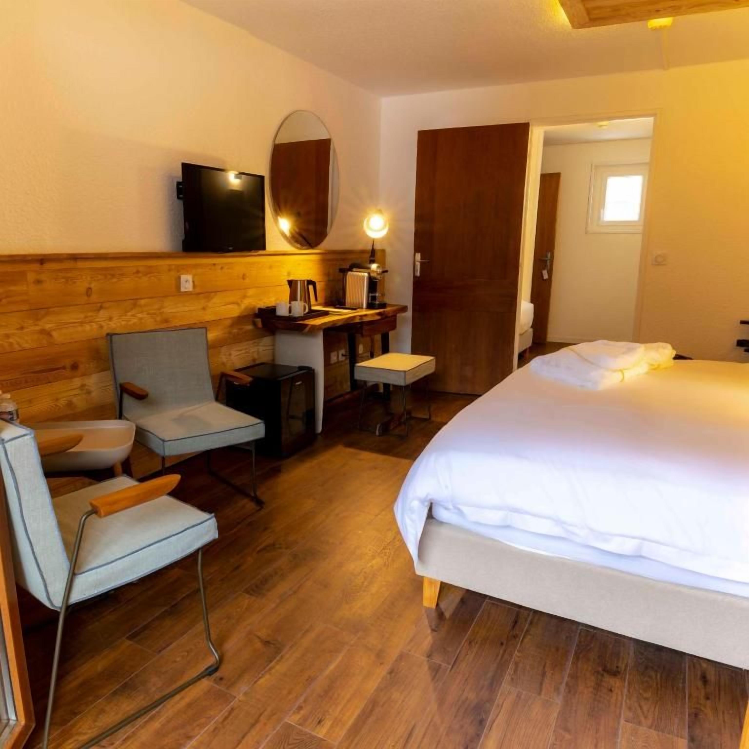 A hotel room with a bed, a seating area with chairs, a television, a mirror, and a wooden wall.