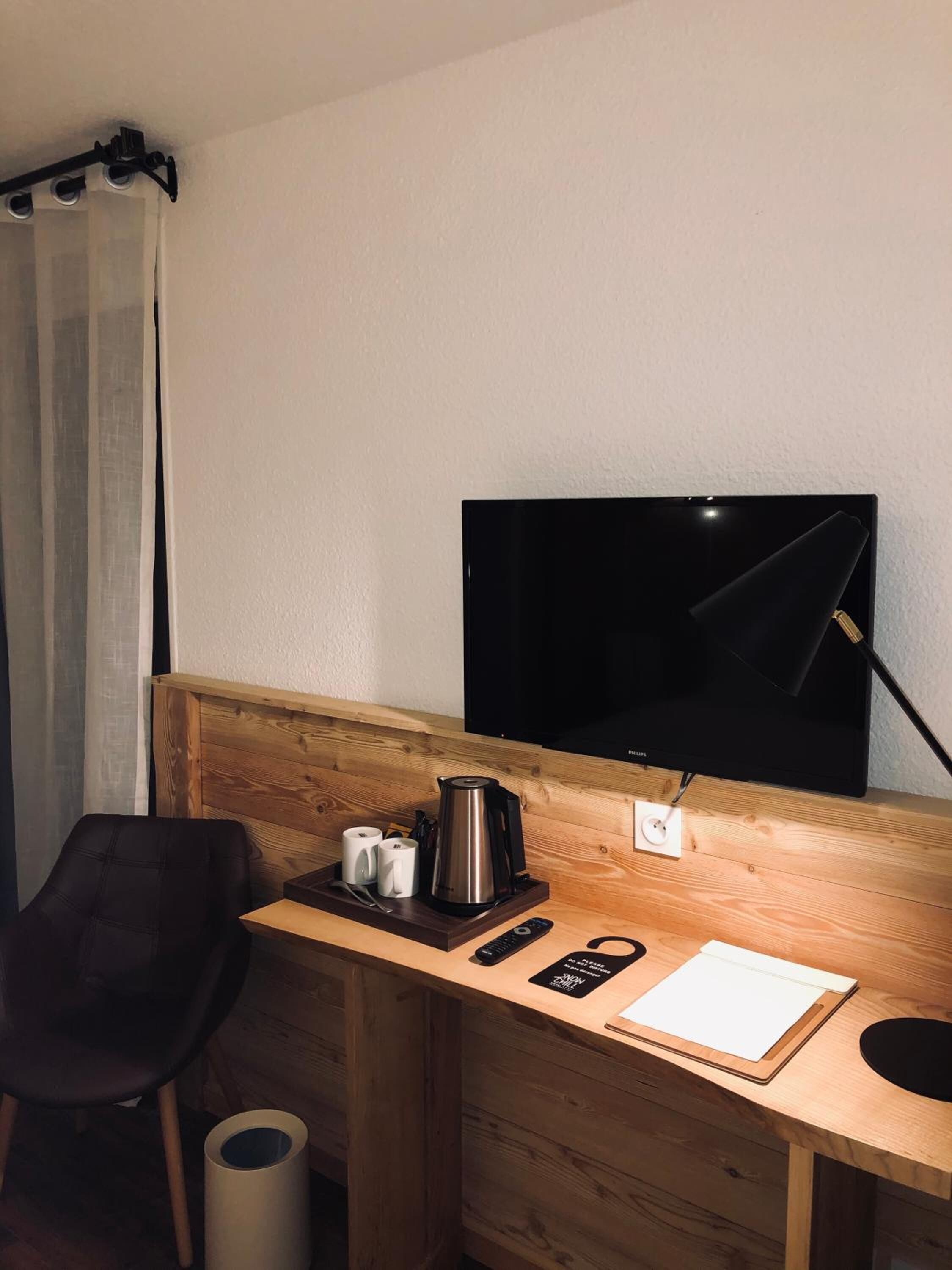 Une chambre d’hôtel compacte comprenant un bureau en bois, un téléviseur noir, une machine à café et une poubelle.