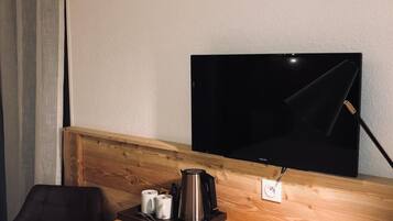 Une chambre d’hôtel compacte comprenant un bureau en bois, un téléviseur noir, une machine à café et une poubelle.