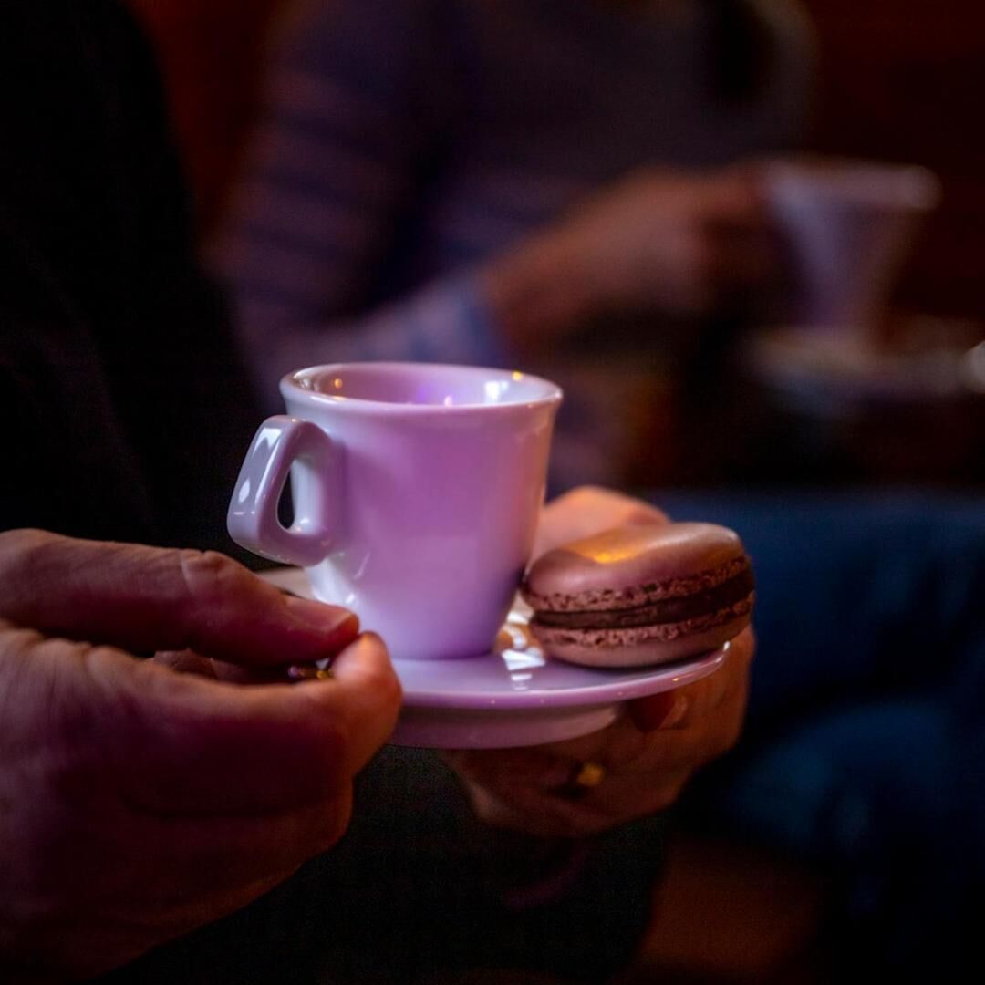 Iemand houdt een paars kopje en een macaron vast.