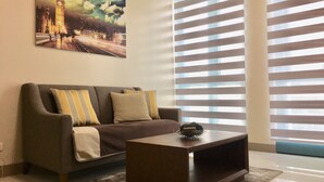 A living room with a sofa, a coffee table, and a painting of a cityscape. - BGC One Uptown 1 Bedroom Corner Unit 16th floor with City View (Taguig)