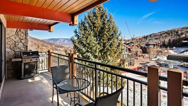 Un balcone con una griglia, due sedie e vista su un paesaggio innevato e degli edifici.