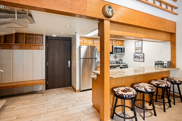 A modern kitchen with wooden accents, a stainless steel refrigerator, and a bar area with stools.