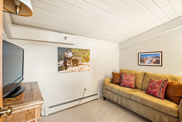 A living room with a TV, a beige sofa with patterned cushions, and two framed pictures on the wall. - 1 Bdrm and Loft, 2 BA Stonebridge Condo 727, Enclosed Loft & bonus room (Snowmass Village)