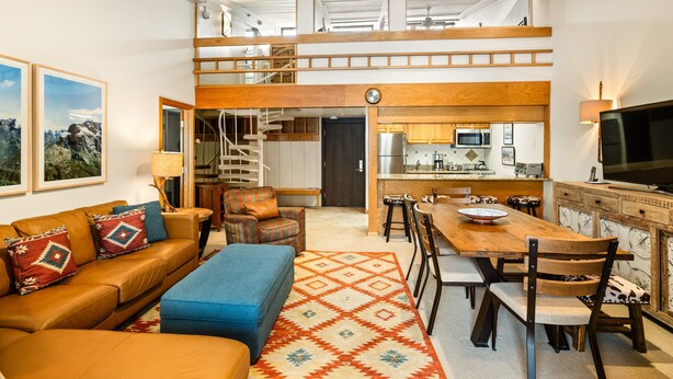 A spacious living area with a high ceiling, a wooden staircase, a kitchen with modern appliances, and a large TV. - 1 Bdrm and Loft, 2 BA Stonebridge Condo 727, Enclosed Loft & bonus room (Snowmass Village)