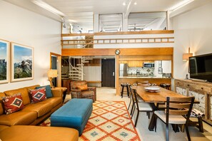 A spacious living area with a high ceiling, a wooden staircase, a kitchen with modern appliances, and a large TV. - 1 Bdrm and Loft, 2 BA Stonebridge Condo 727, Enclosed Loft & bonus room (Snowmass Village)