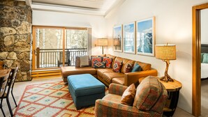 A cozy living room with a stone wall, a large window, a sofa set, a patterned rug, and a side table with a lamp. - 1 Bdrm and Loft, 2 BA Stonebridge Condo 727, Enclosed Loft & bonus room (Snowmass Village)