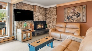 Ein Wohnzimmer mit Steinwand, Kamin, Ledersofa und einem an der Wand befestigten Fernseher.