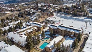 An aerial view of a ski resort with multiple buildings, a swimming pool, and surrounding snowy landscape. - Stonebridge Condos 707 1 Bdrm Slopeside (Snowmass Village)