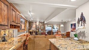 A spacious kitchen with granite countertops, wooden cabinets, and a stone accent wall. - Stonebridge Condos 707 1 Bdrm Slopeside (Snowmass Village)