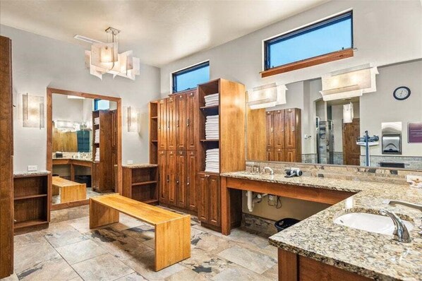 A bathroom with wooden cabinets, a granite countertop sink, and a bench.